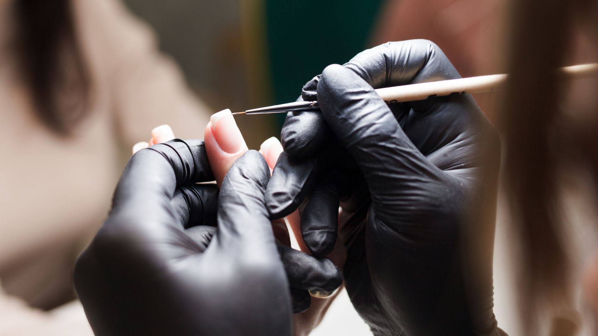 A close-up of gloved hands carefully applying nail polish with a thin brush to someone’s fingernails, suggesting a manicure in progress—attention to detail you’d expect from a personal injury attorney Abilene Texas relies on. The background is softly blurred.